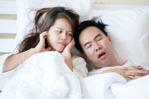Man snoring while woman covers her ears